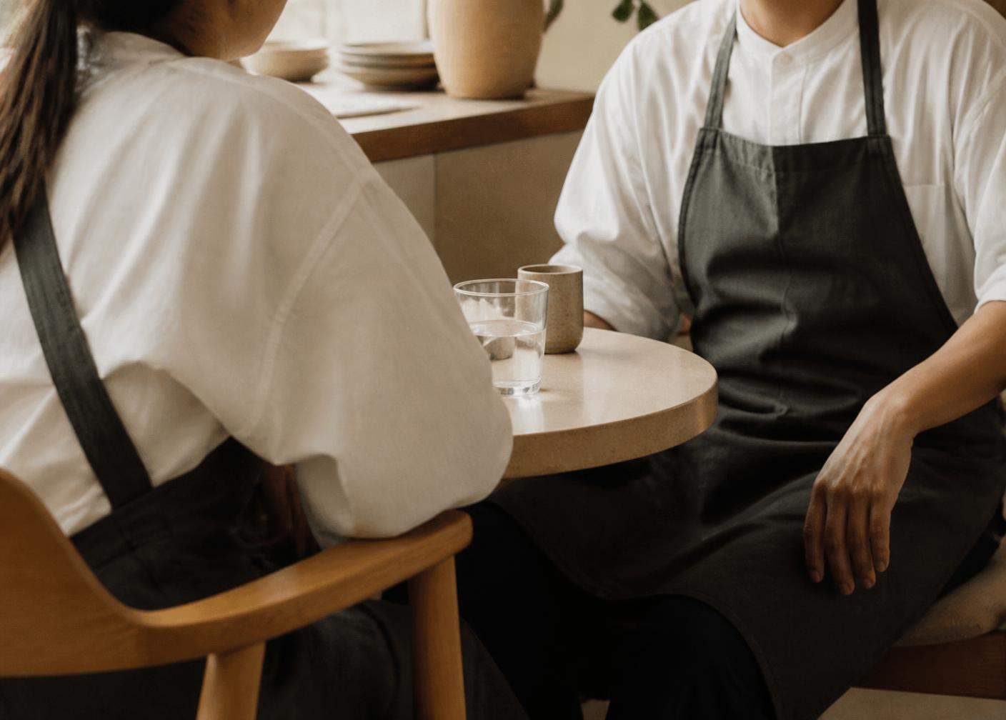 Two hospitality professionals in conversation across a table in a warm, light-filled room